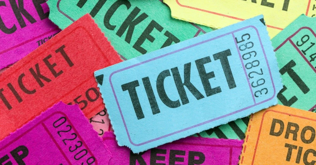Close-up of a pile of bright purple, blue, green, and yellow paper raffle-style tickets. A blue ticket is in the center.