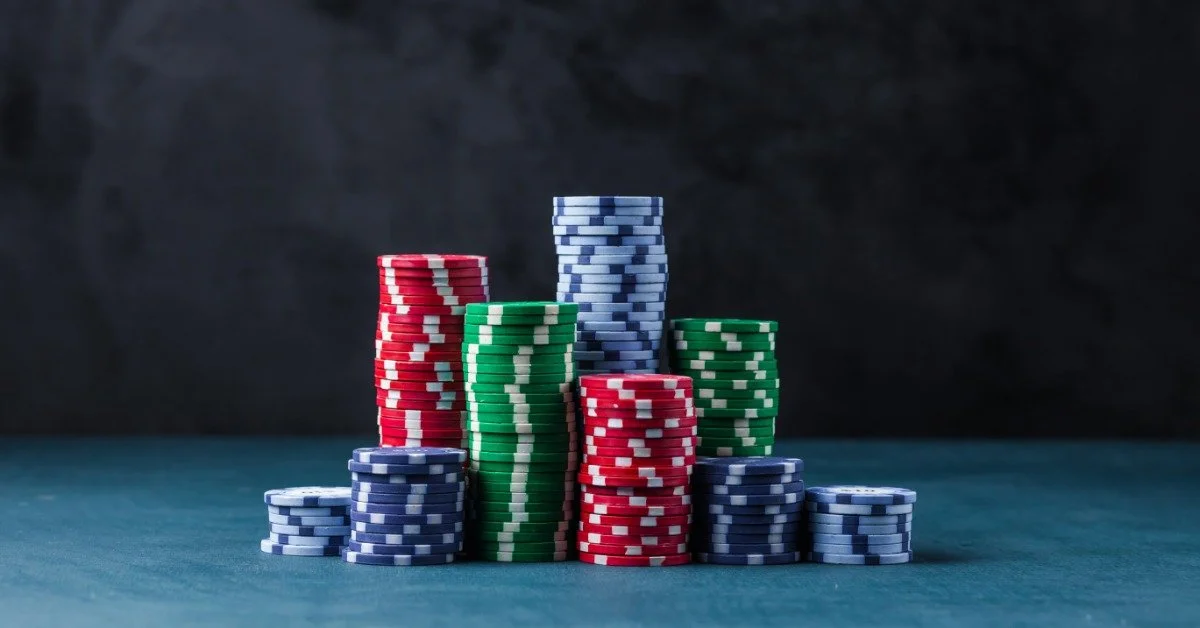 Stacks of red, green, and blue casino chips are arranged on a blue tabletop in front of a dark, textured background.