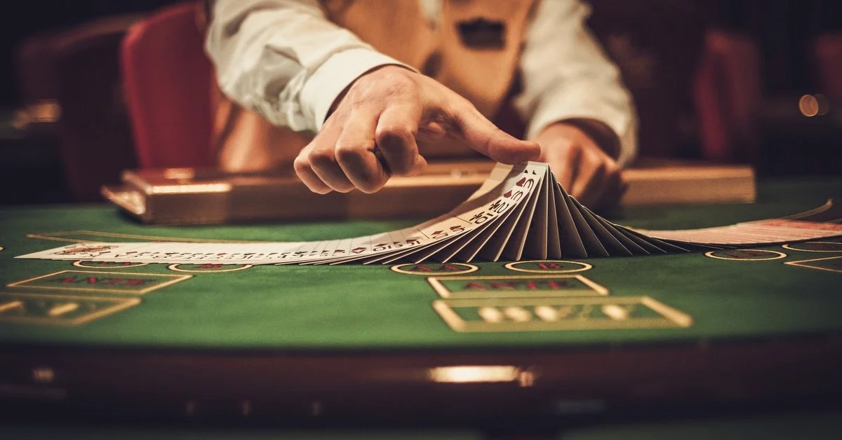 A dealer touches playing cards that are fanned out on a green felt table. The table is lit, and the background is dim.