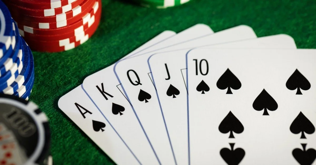 A royal flush in spades is fanned out across a green felt table. Colorful casino chips are stacked around the cards.