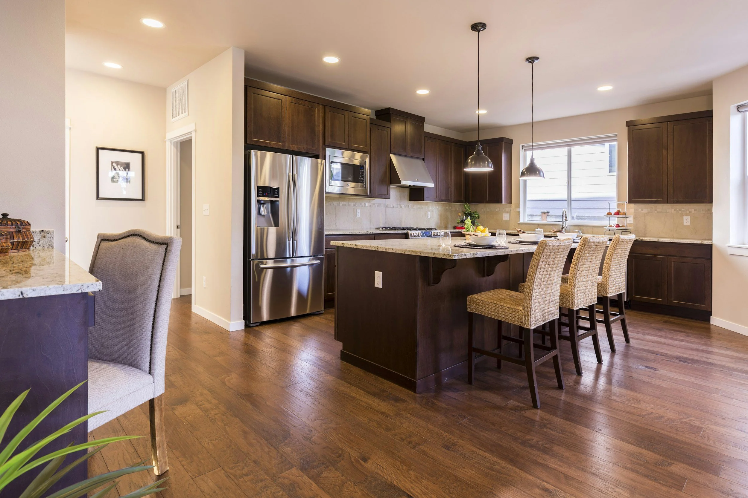 Modern kitchen with dark wood cabinets, stainless steel refrigerator, microwave, and oven, island with seating, pendant lights, and hardwood flooring.