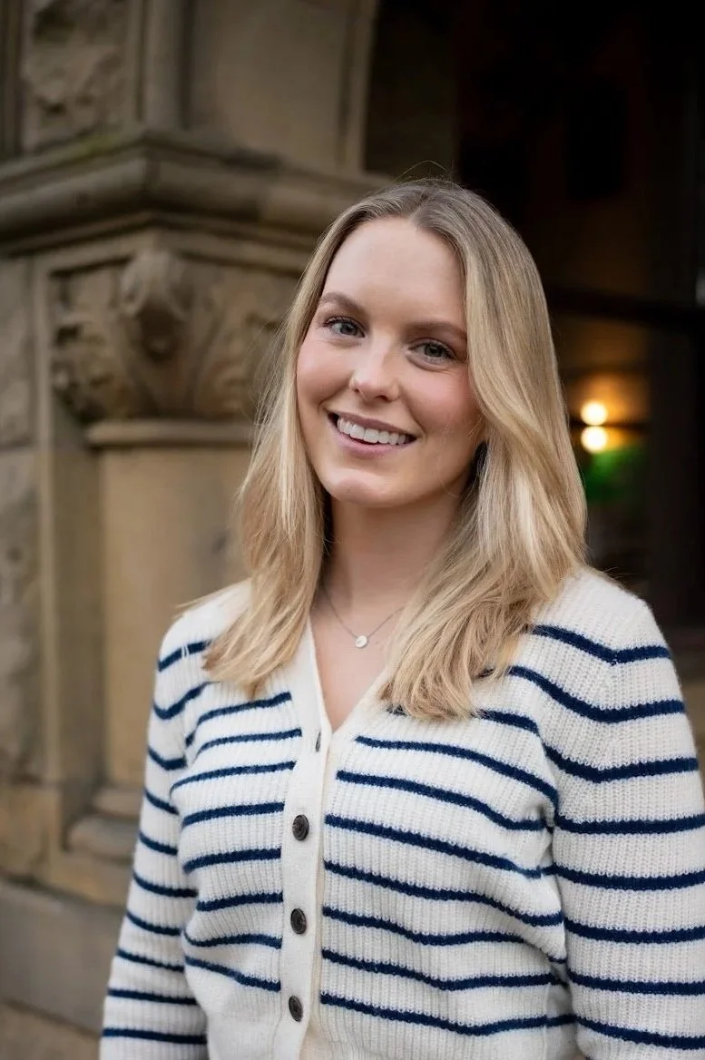 A compassionate, female therapist with blonde hair smiling outdoors near a stone building in San Francisco, Califnornia