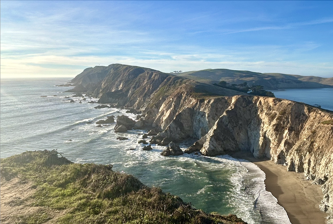 Coastal cliffs with a sandy beach below, ocean waves, and blue sky. Mindful space, nature therapy