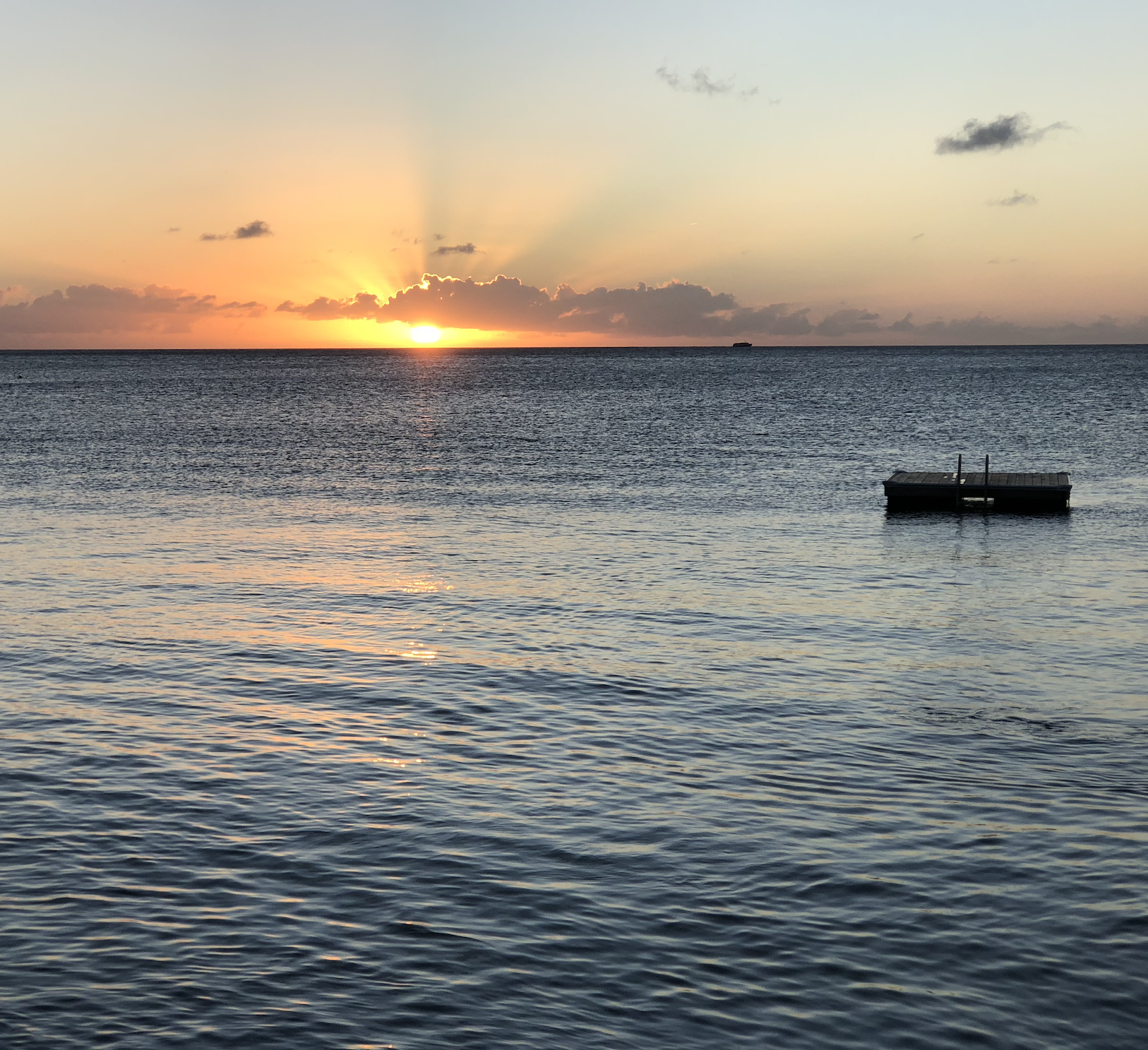 photograph of sunset over the ocean, with the sun partially behind clouds, and small dock floating on the water in the foreground. Offers calming and contemplative space to match space of compassionate therapy for anxiety in California