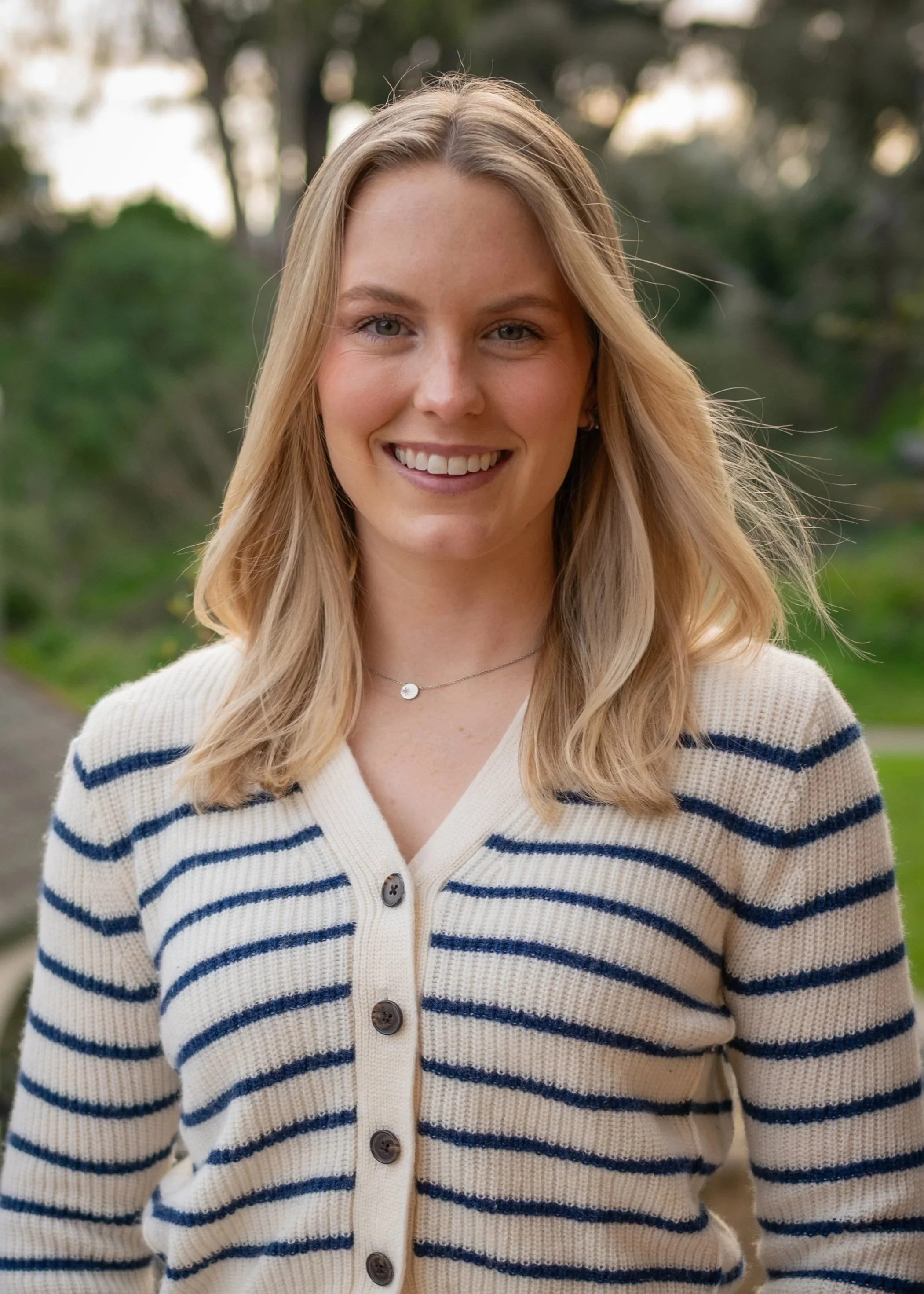 A young female therapist with blonde hair and blue eyes smiling outdoors, wearing a cream-colored cardigan in San Francisco, California.