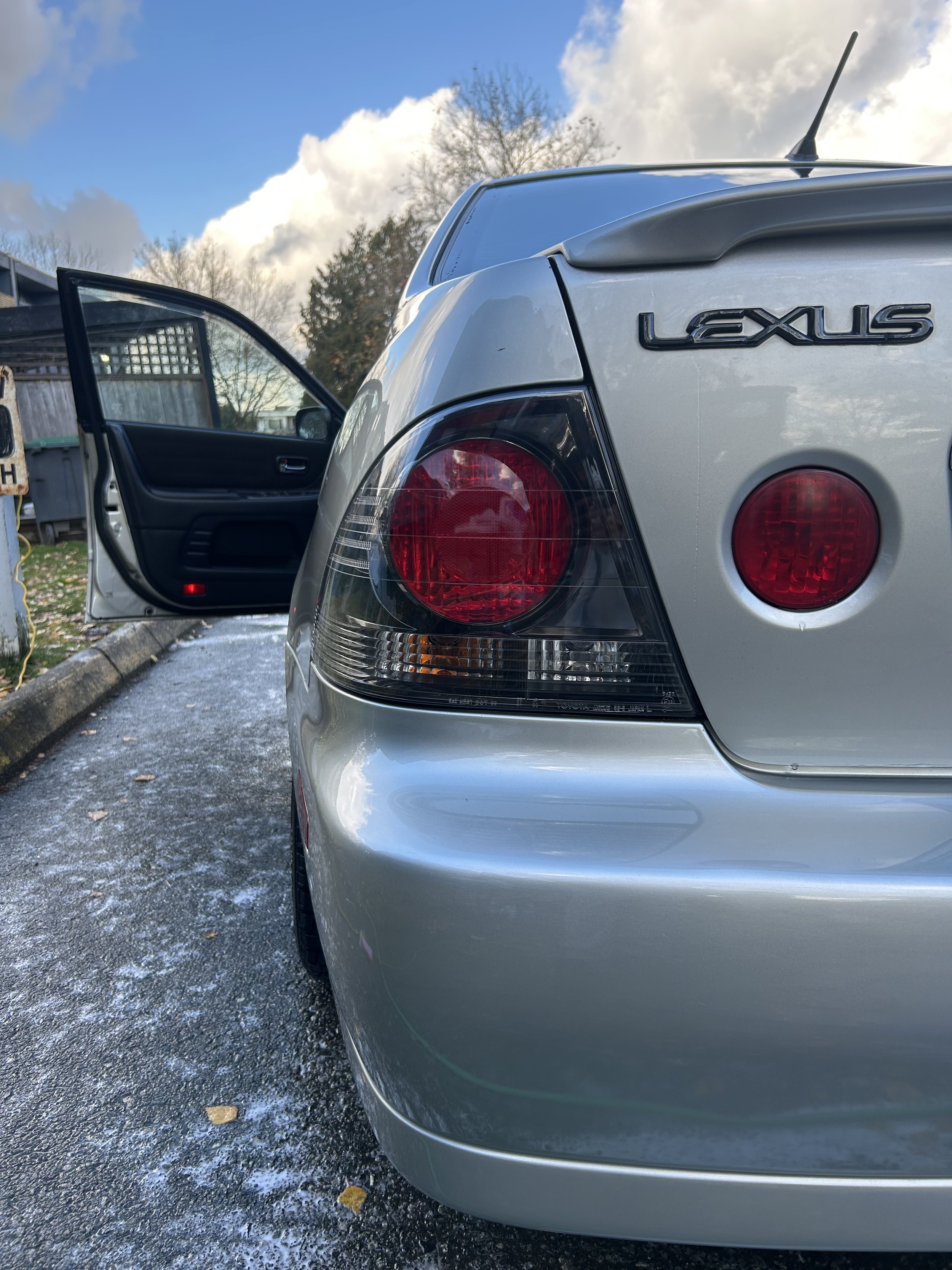 Rear view of a silver Lexus car with an open driver's side door, parked on a frosty driveway.