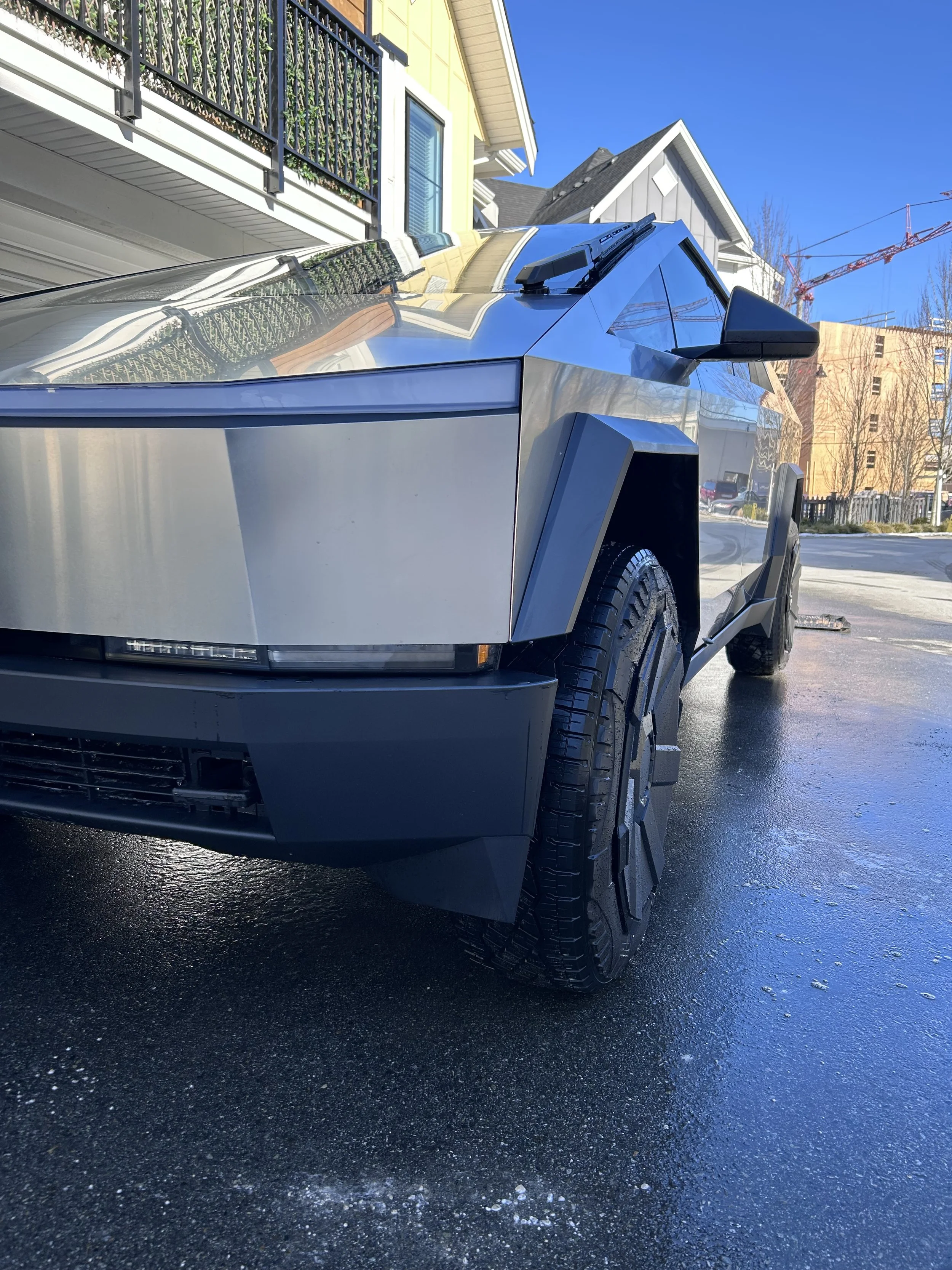 Futuristic electric truck parked in a residential driveway with a modern design and angular body, reflecting nearby houses.