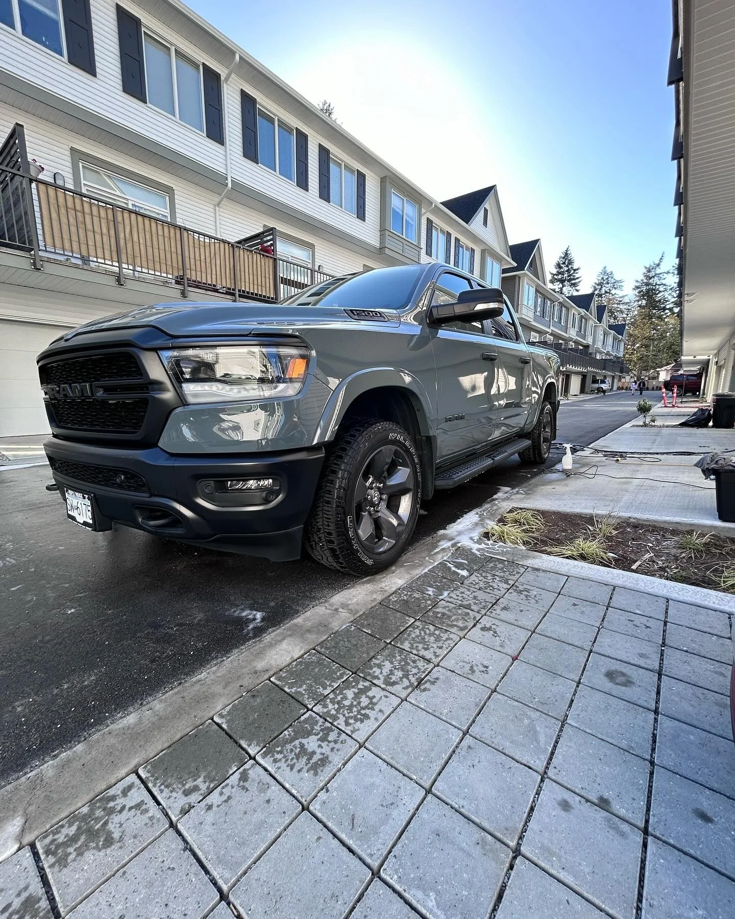 A gray pickup truck parked in front of a row of modern townhouses on a sunny day.