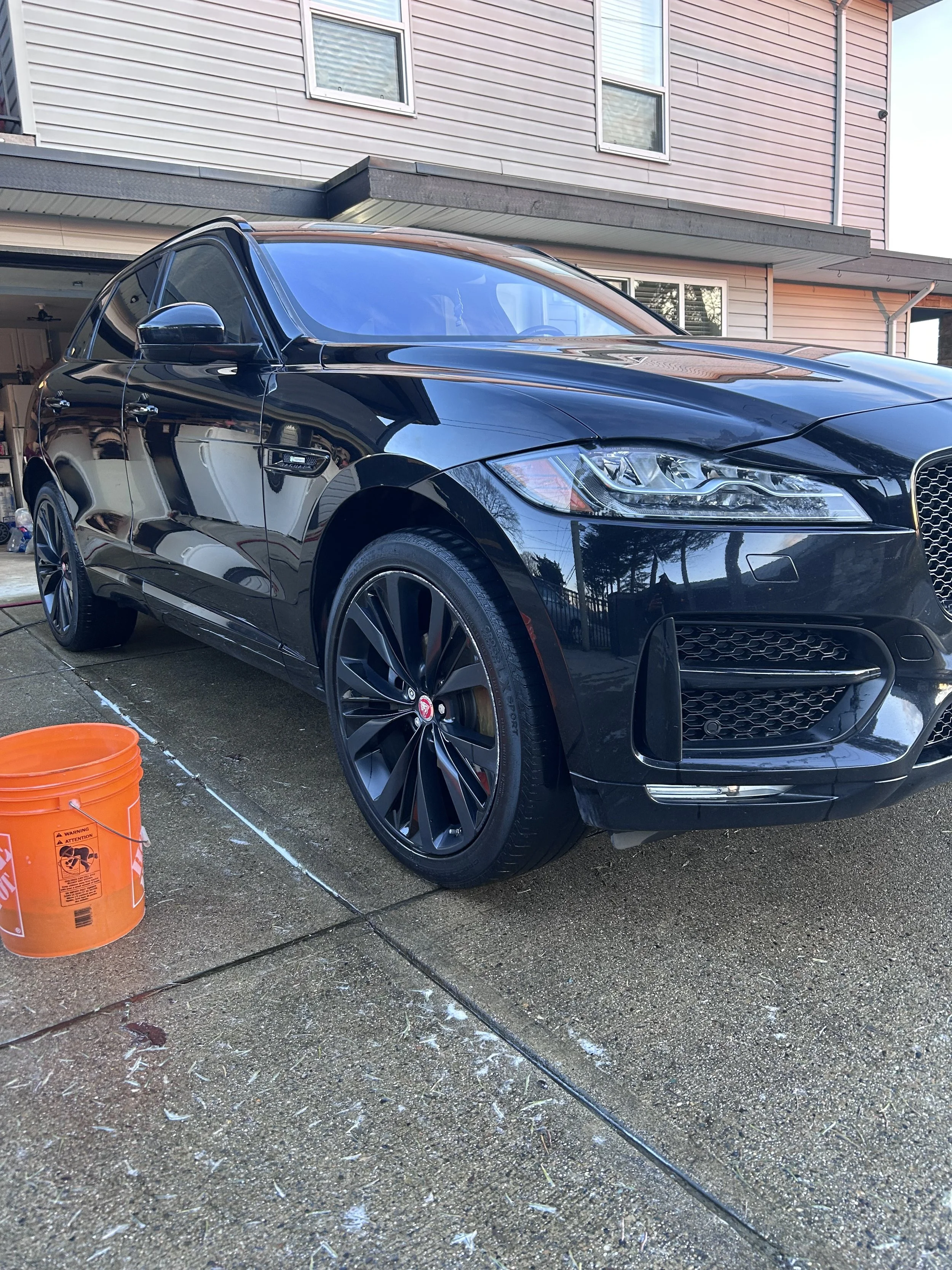 Black SUV parked in driveway near an orange bucket, in front of a house.