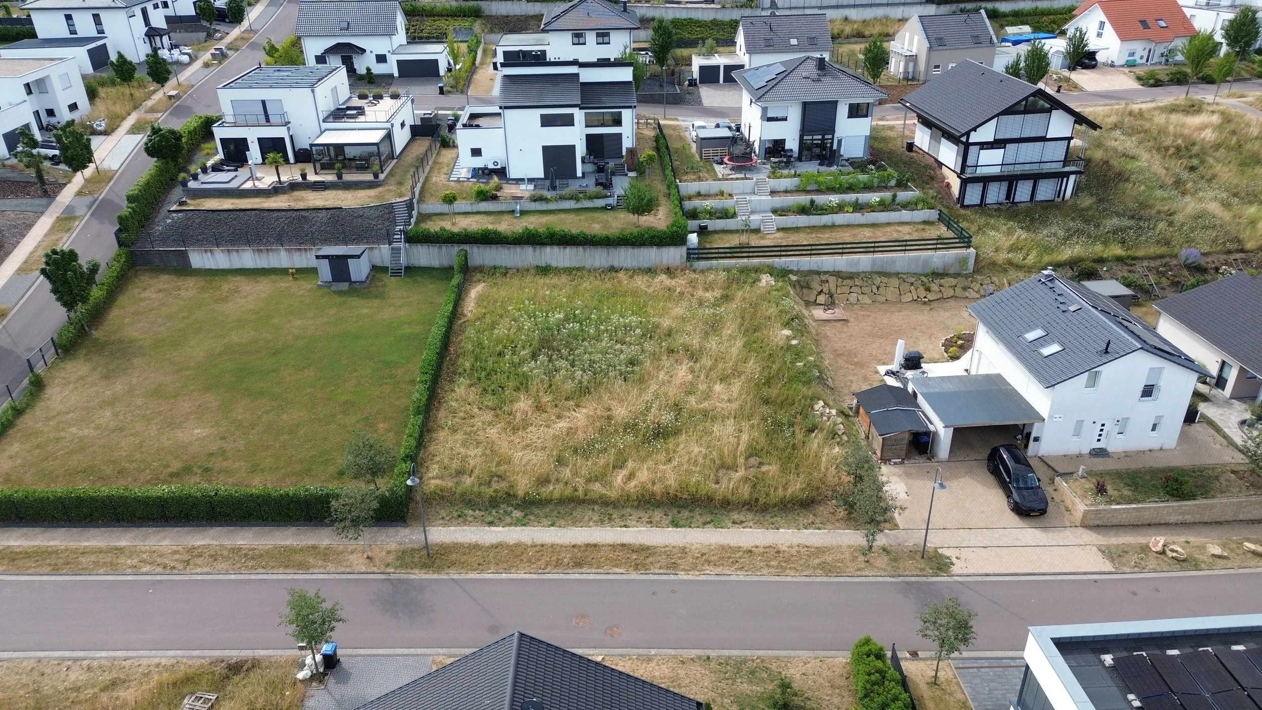 Vue aérienne d'une zone résidentielle avec plusieurs maisons modernes, jardins, et rues pavées.