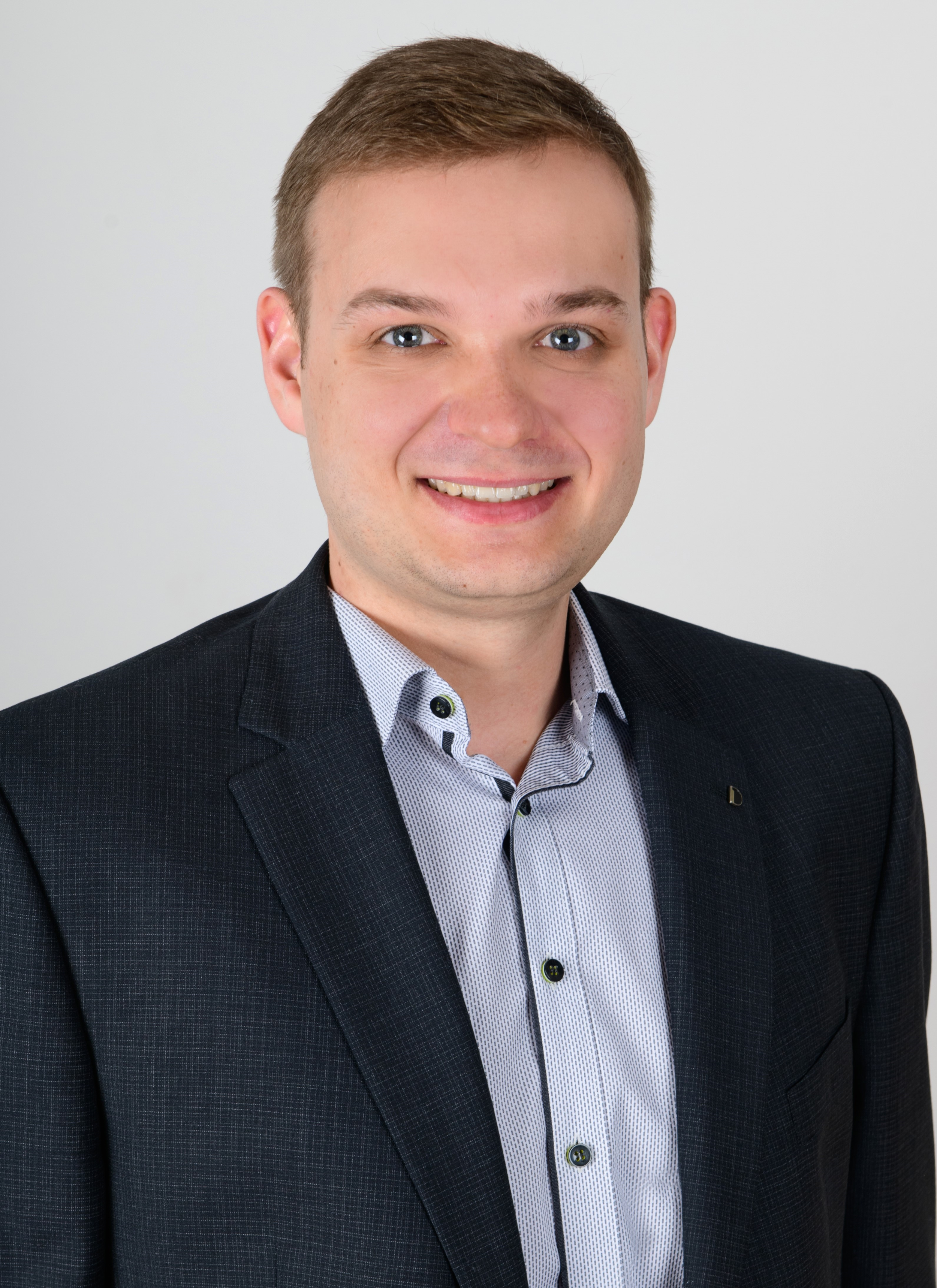 Un homme souriant en costume cravate devant un fond blanc.