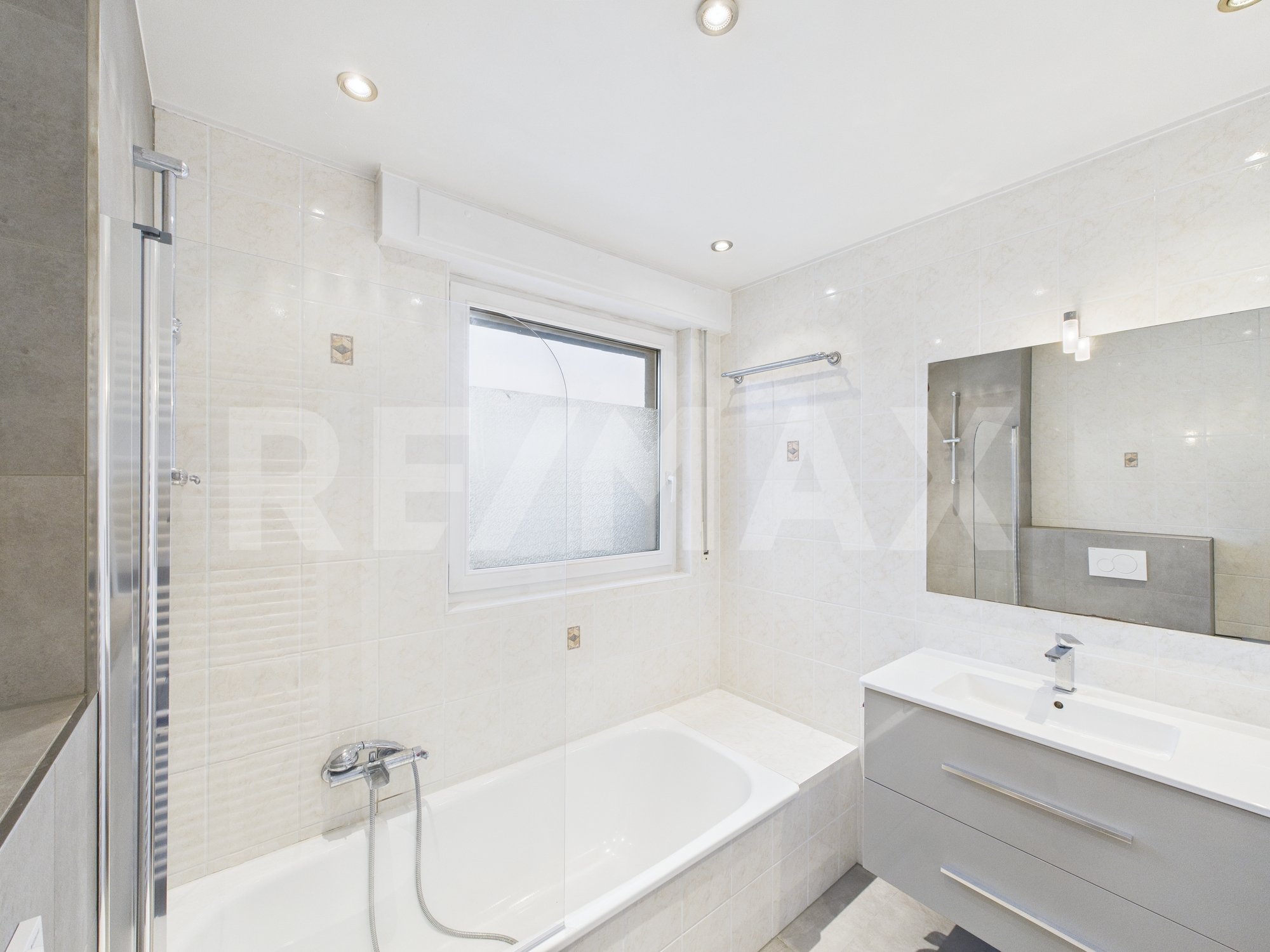 Salle de bain moderne avec baignoire, lavabo, miroir, fenêtre et éclairage encastré.