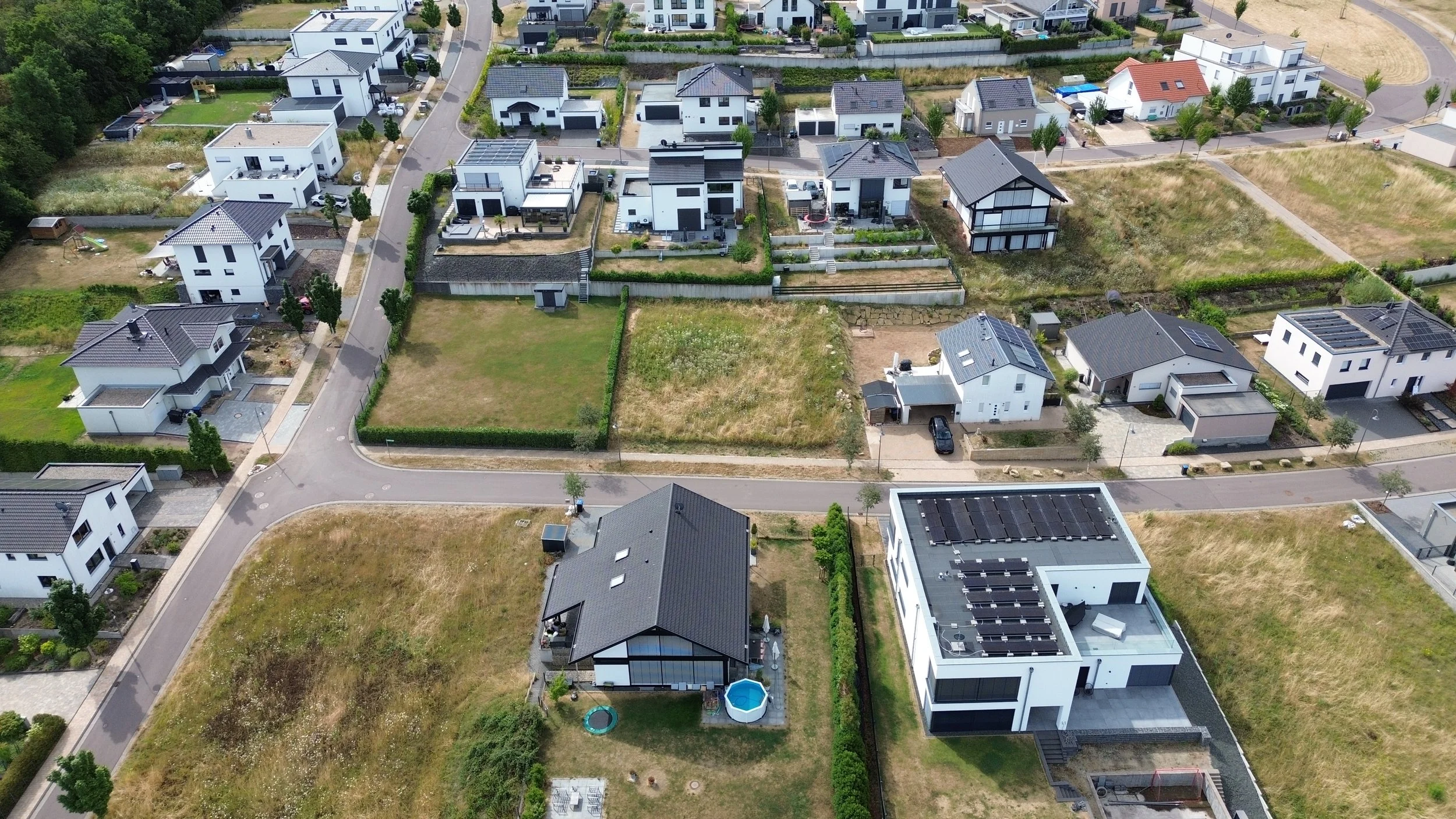 Vue aérienne d'un quartier résidentiel avec plusieurs maisons modernes, jardins, et routes bordées d'arbres.