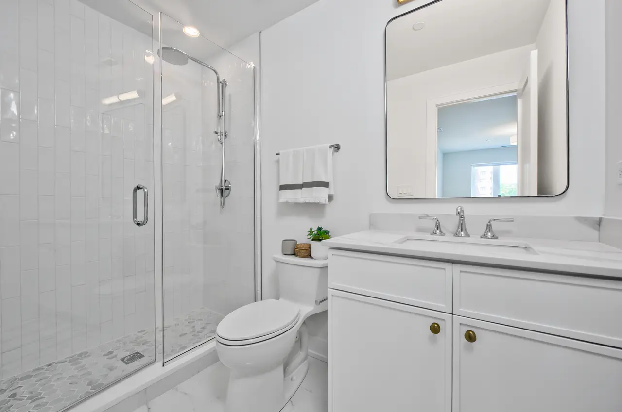 Modern bathroom with a glass-enclosed shower, white vanity with a mirror, toilet, and minimal decor.