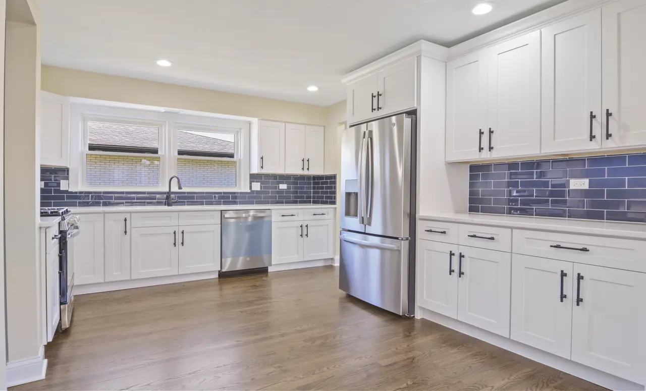 Modern kitchen with white cabinets, stainless steel appliances, blue subway tile backsplash, and hardwood floors.
