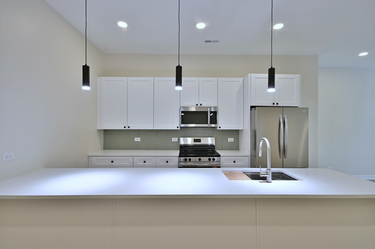 Modern kitchen with white cabinets, stainless steel appliances, pendant lights, and a white island countertop.