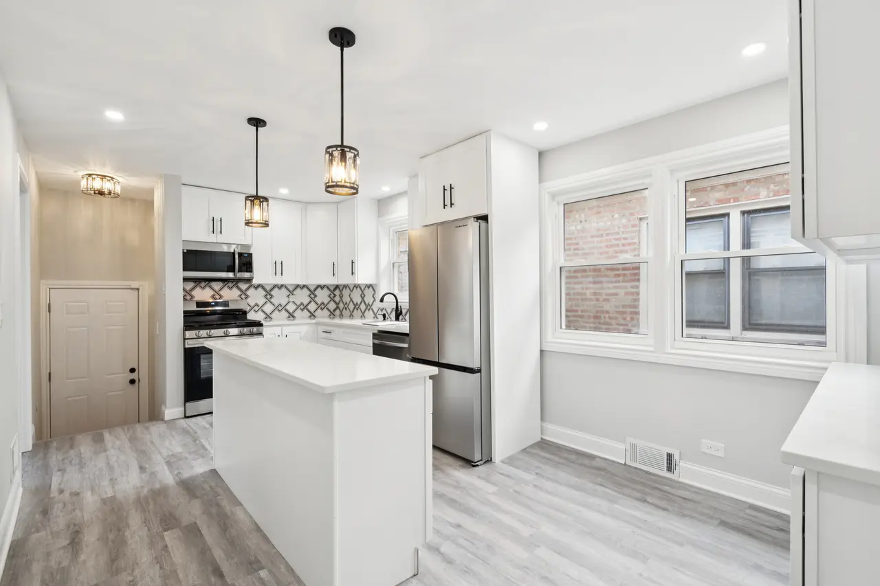 Modern kitchen with white cabinets, stainless steel appliances, patterned backsplash, central island, and large double window brightening the space.