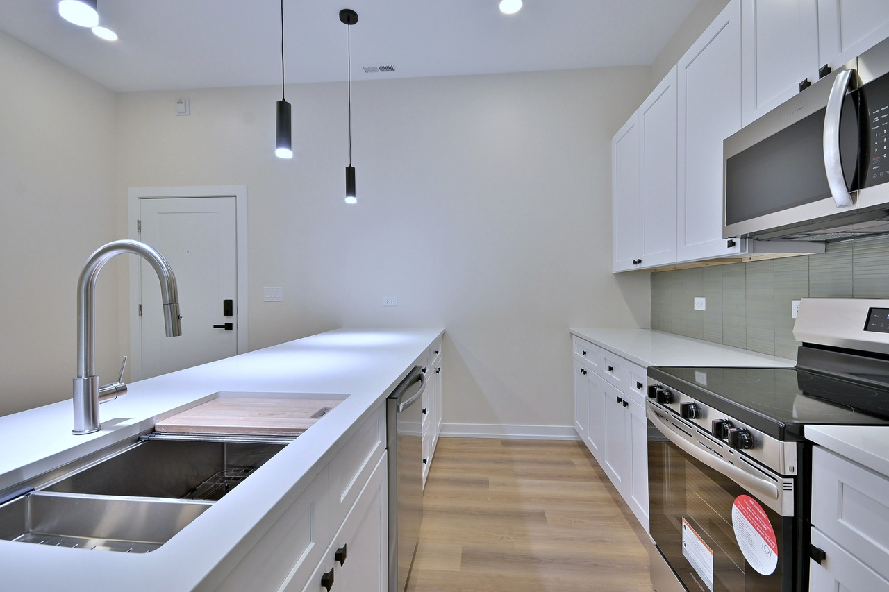Modern kitchen with white cabinets, stainless steel appliances, a white countertop island, a black stove, a microwave, a stainless steel sink, and black pendant lights.