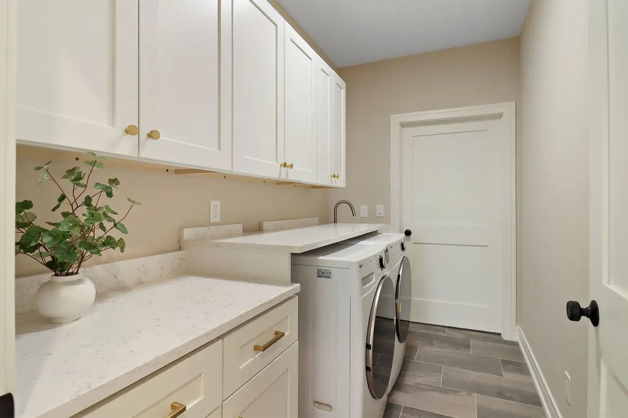 Laundry room with white cabinets, a white countertop, a washing machine, and a small potted plant.