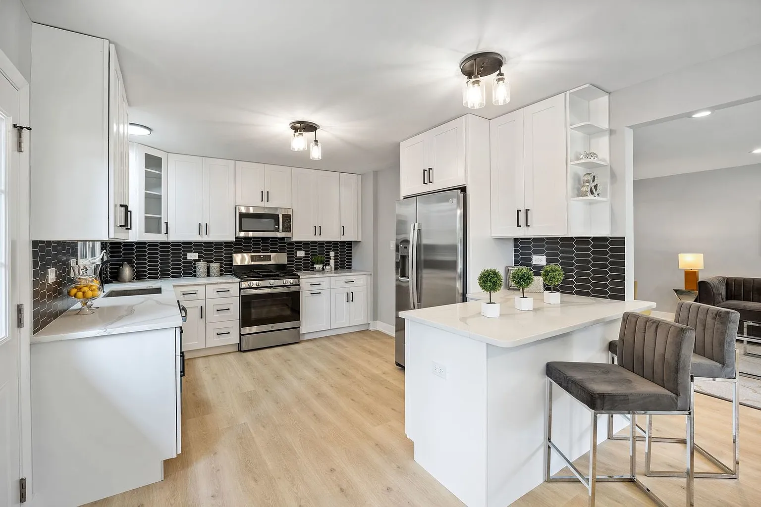 Modern kitchen with white cabinets, black tile backsplash, stainless steel appliances, and a breakfast bar with gray chairs.