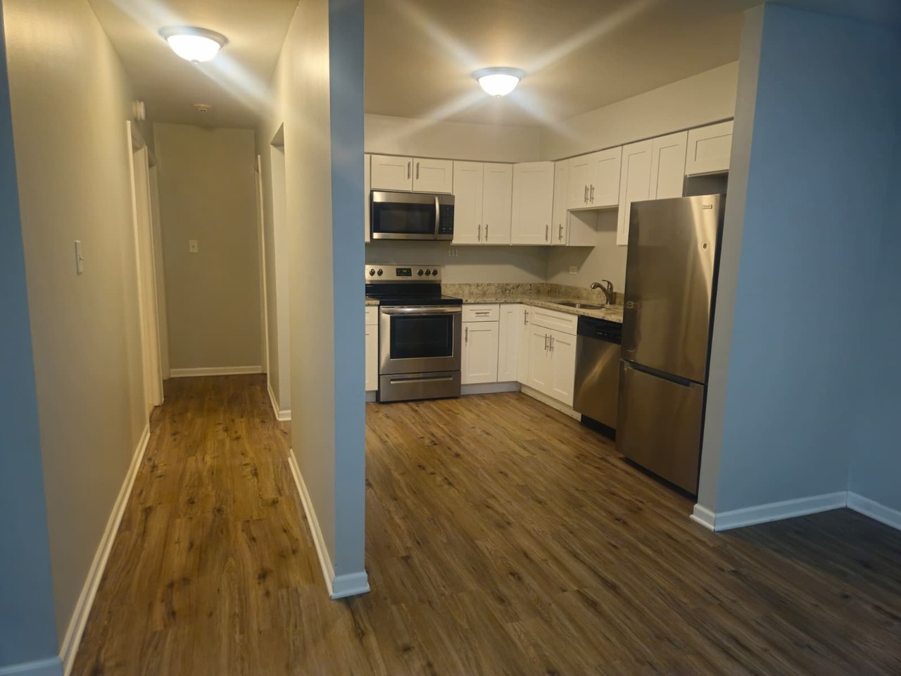 Kitchen with white cabinets, stainless steel appliances, granite countertops, and wood flooring.