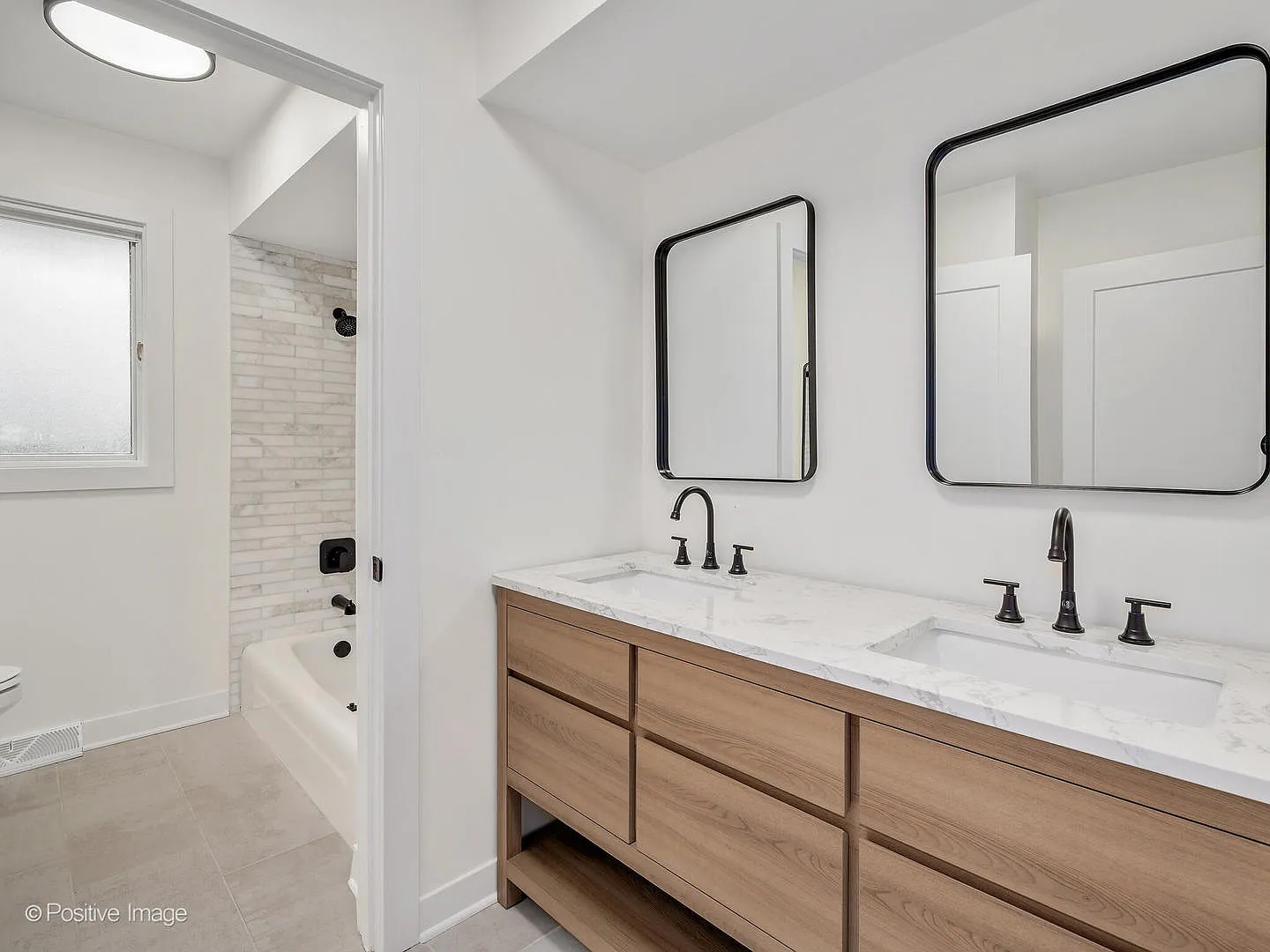 Modern bathroom with double sink vanity, black-framed mirrors, and a shower with frosted window and white brick tiles.