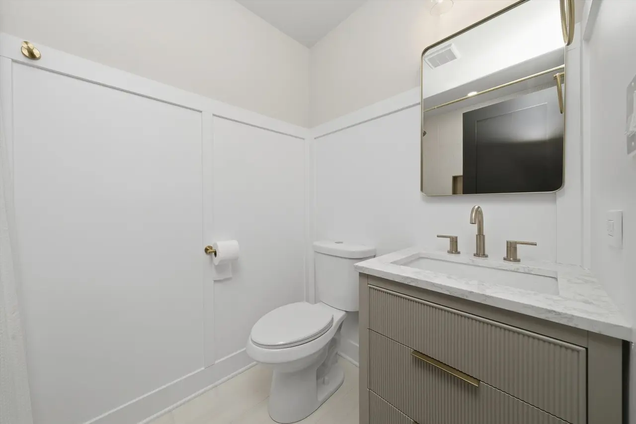 Modern small bathroom with white walls, white toilet, and a gray vanity with a marble countertop, a gold faucet, and a rectangular mirror.