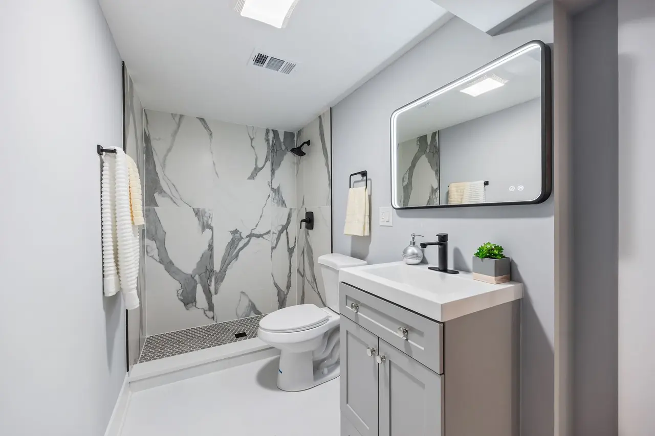 Modern bathroom with a marble shower, white toilet, gray vanity with a mirror, black faucet, and a small plant.