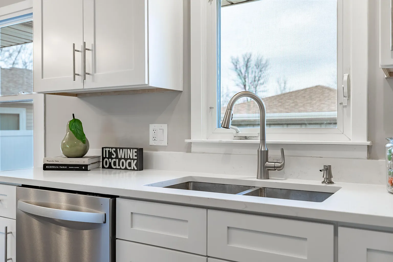 Kitchen with white cabinets, stainless steel dishwasher, double sink, silver faucet, and a window overlooking a yard.