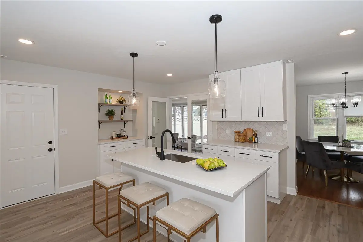 Open concept kitchen with white cabinets, island with seating, and a dining area with large windows.