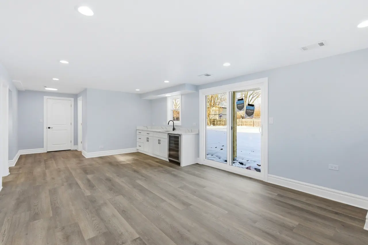 Empty living area with light blue walls, wood flooring, and sliding glass door leading to a snowy backyard with trees.