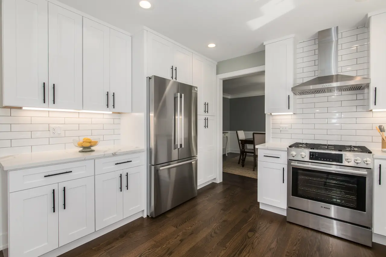 Modern kitchen with white cabinets, stainless steel refrigerator and stove, white subway tile backsplash, and dark hardwood floors.