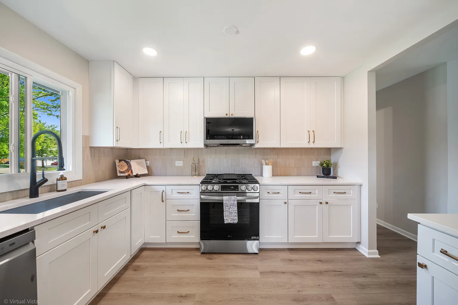 Modern kitchen with white cabinets, black stove, and stainless steel appliances. Natural light from a window over the sink.