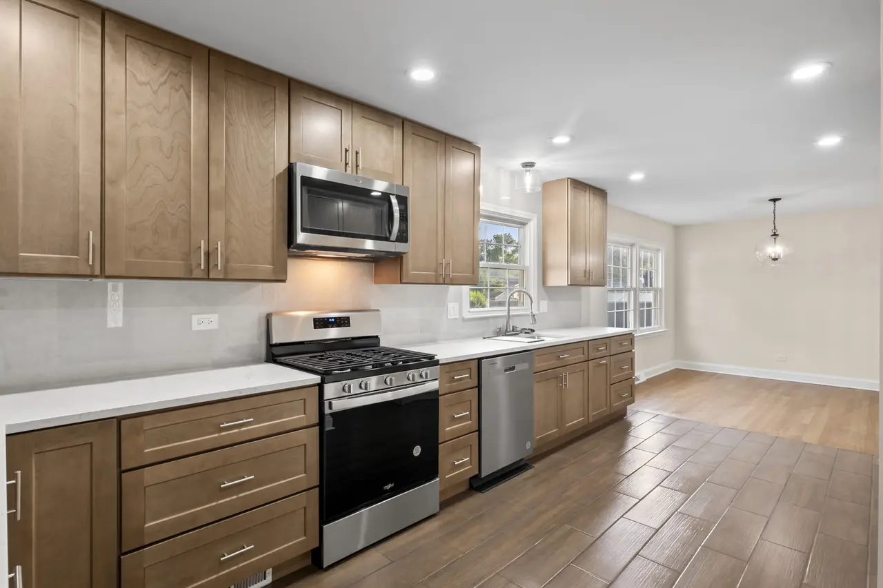 Modern kitchen with wooden cabinets, stainless steel oven and microwave, white countertops, hardwood and tile floors, and large windows with views.