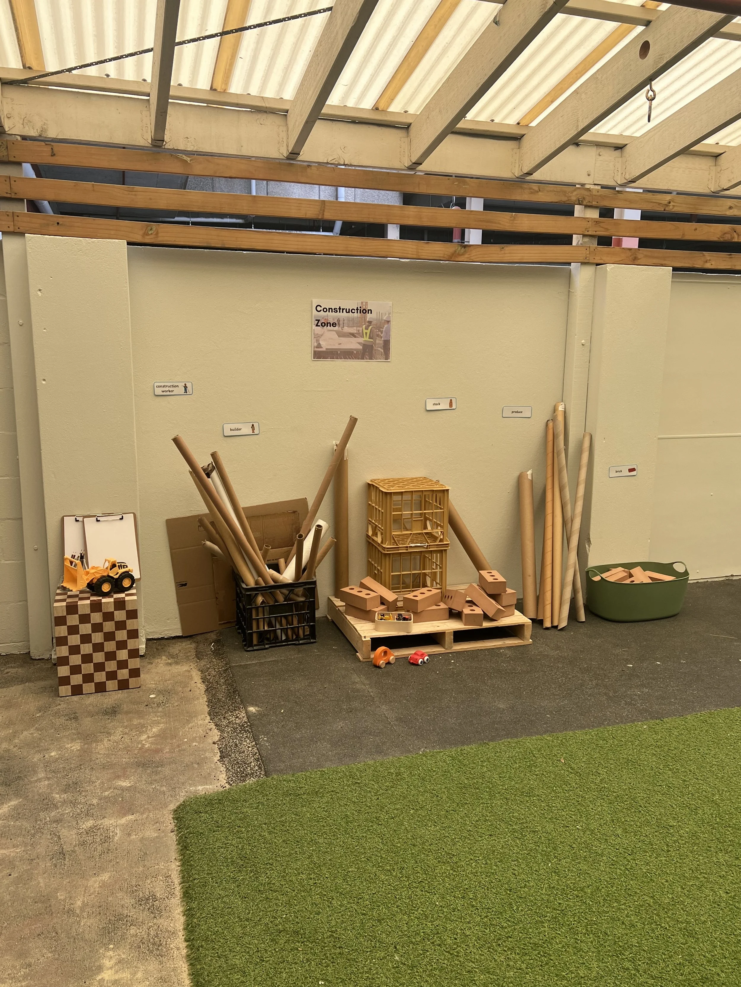 Indoor construction-themed play area with toy construction equipment, bricks, and building materials, separated by a wall labeled 'Construction Zone'.