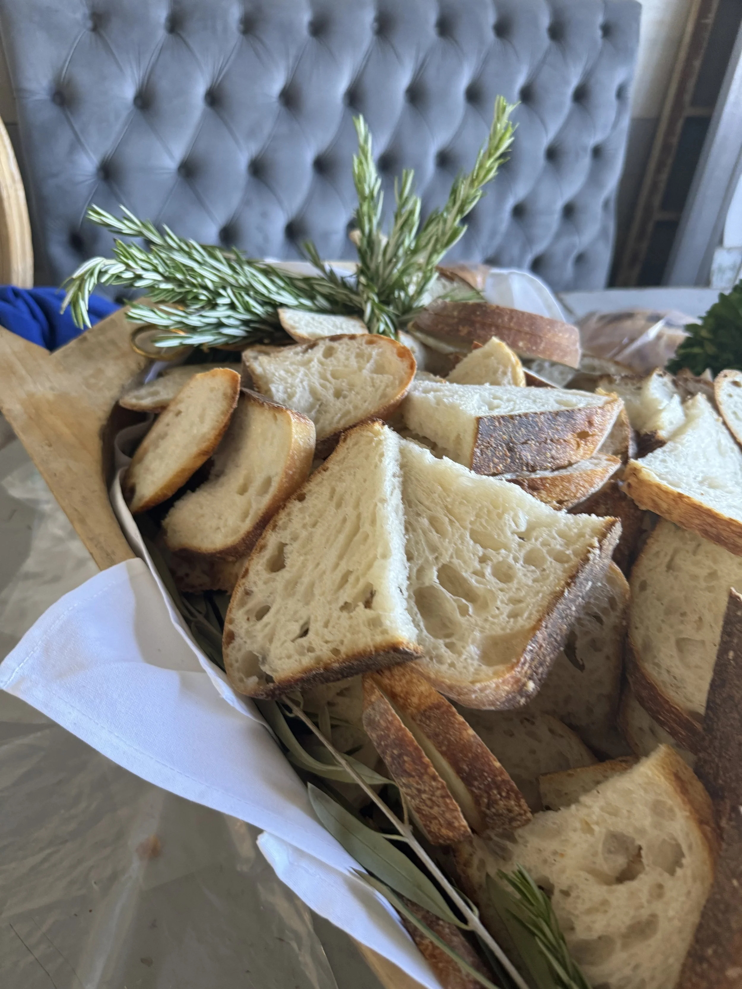 Slices of rustic bread with rosemary garnish on a wooden tray.