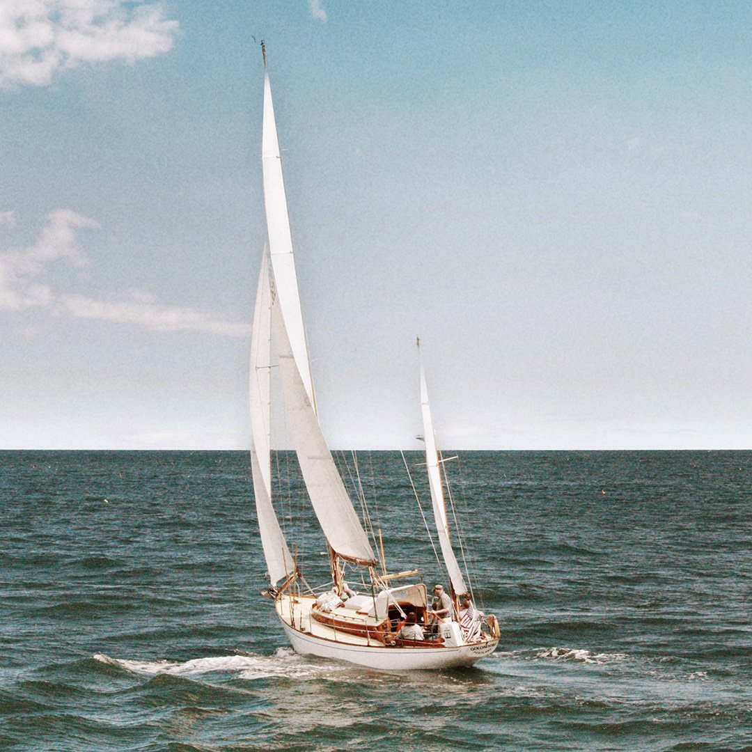 Una barca a vela con tre vele bianche in mare aperto sotto un cielo leggermente nuvoloso.
