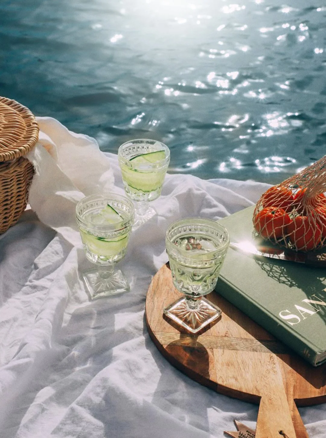 Tre bicchieri di liquore con limone, una cesta con pomodorini e un libro. Scena alla riva del mare.