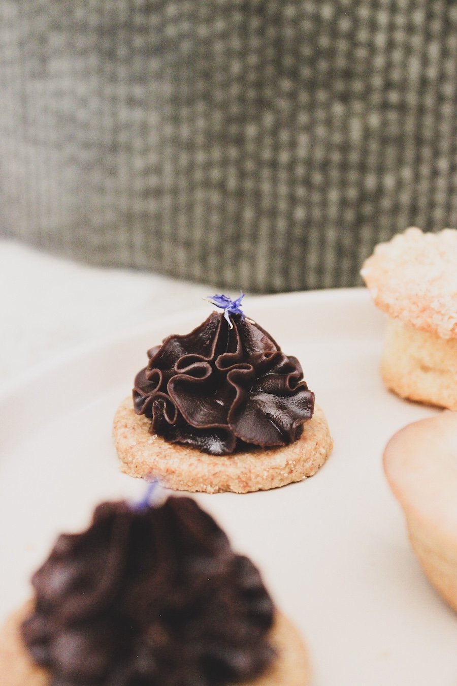 Biscuits décorés de ganache au chocolat et fleur comestible sur une assiette.