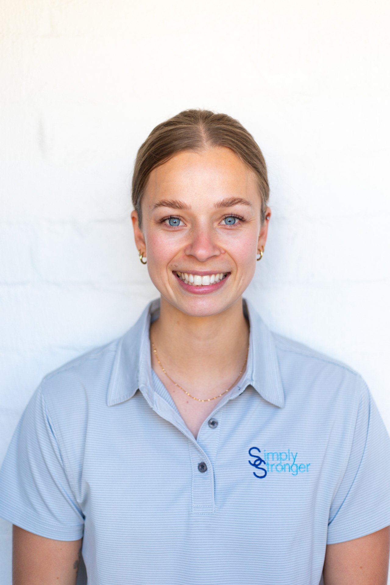 Olivia with long blonde hair in a grey Simply Stronger shirt on a blue back ground.
