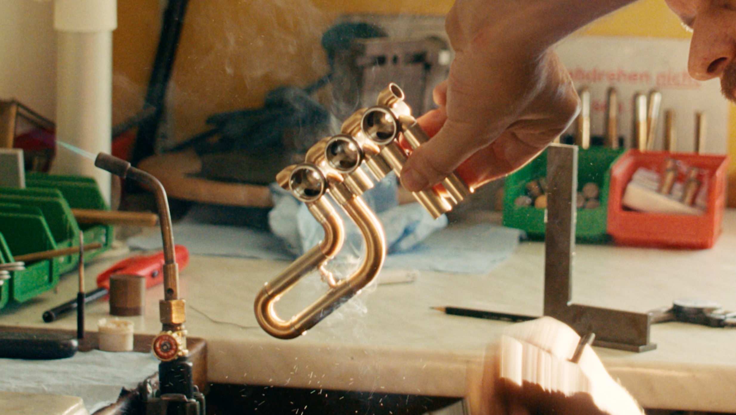 A Schagerl Music GmbH employee, working on a small soldering project at a cluttered workbench, connecting copper pipes and components.