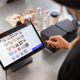 Person using a square register for ordering or browsing food, with beverages in the background.