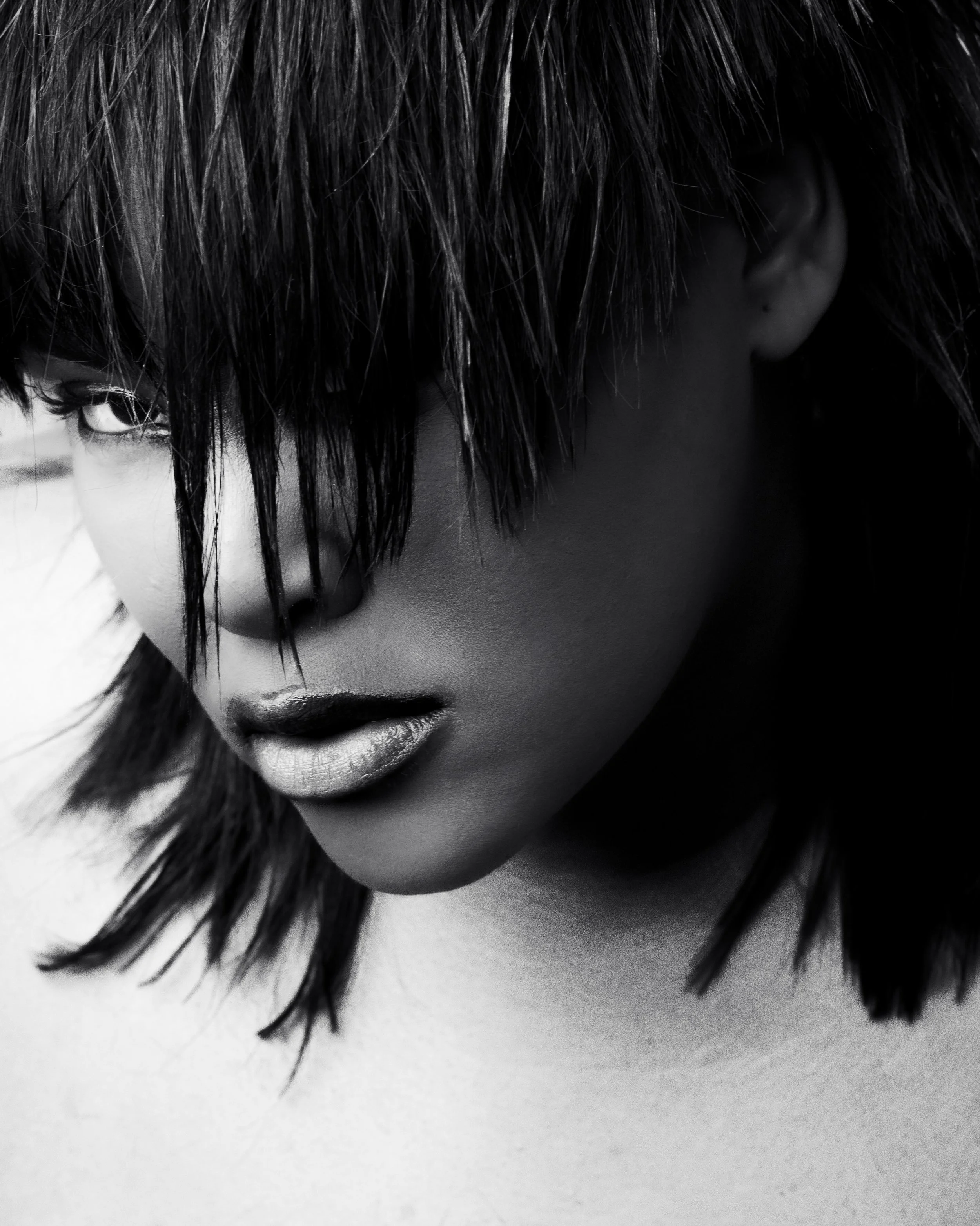 A black-and-white portrait of a woman with dark, tousled hair, looking down, her face partially obscured by strands of hair.