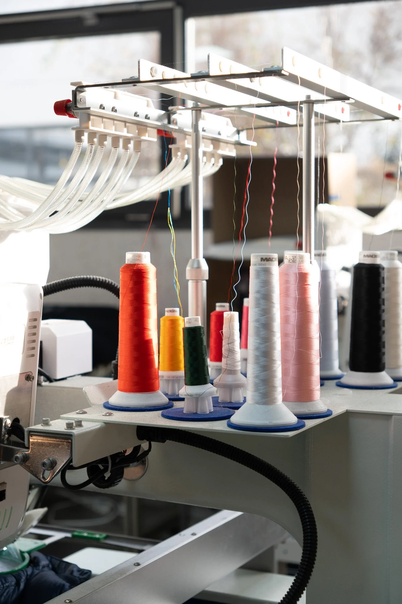 Machine à coudre industrielle avec bobines de fil de différentes couleurs dans un atelier de couture.