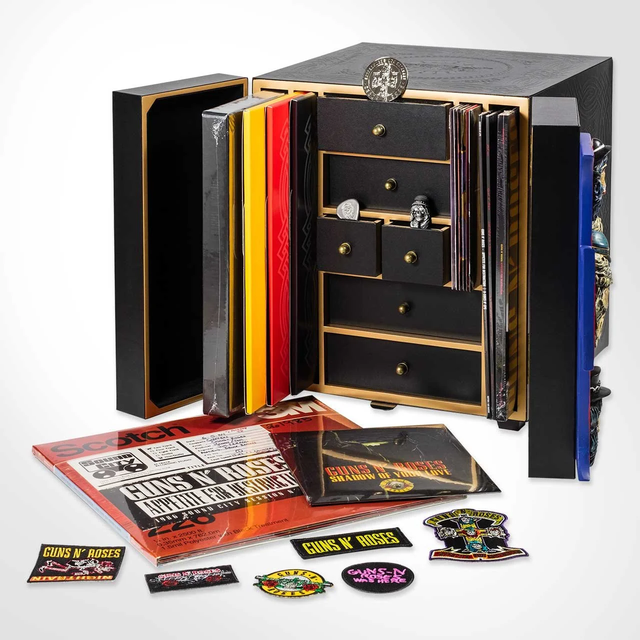 Une boîte à bijoux noire et dorée contenant des magazines et des objets, entourée de plusieurs magazines et patchs du groupe Guns N' Roses.