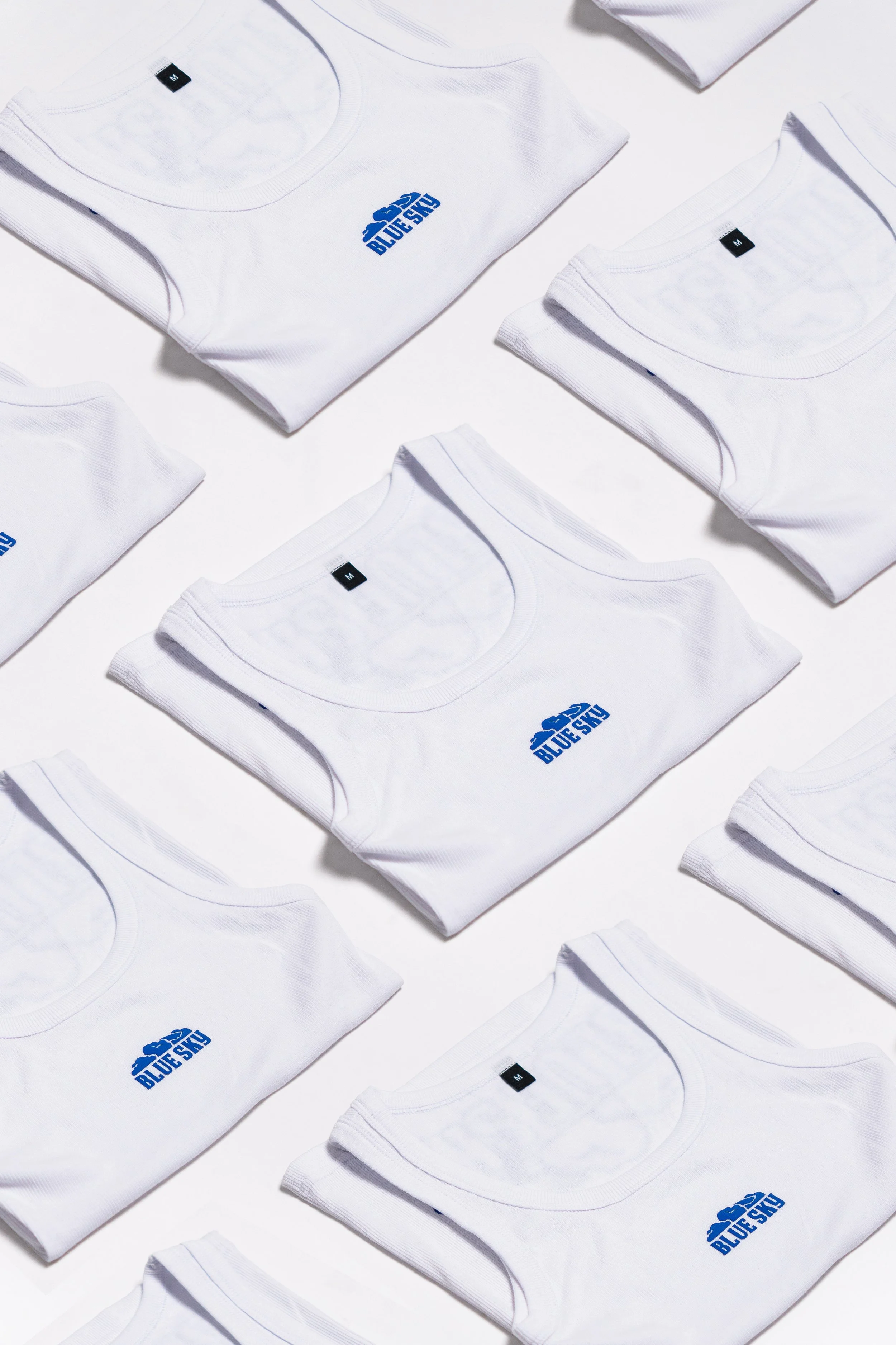 Plusieurs t-shirts blancs pliés avec le logo bleu "Blue Sky" affiché.