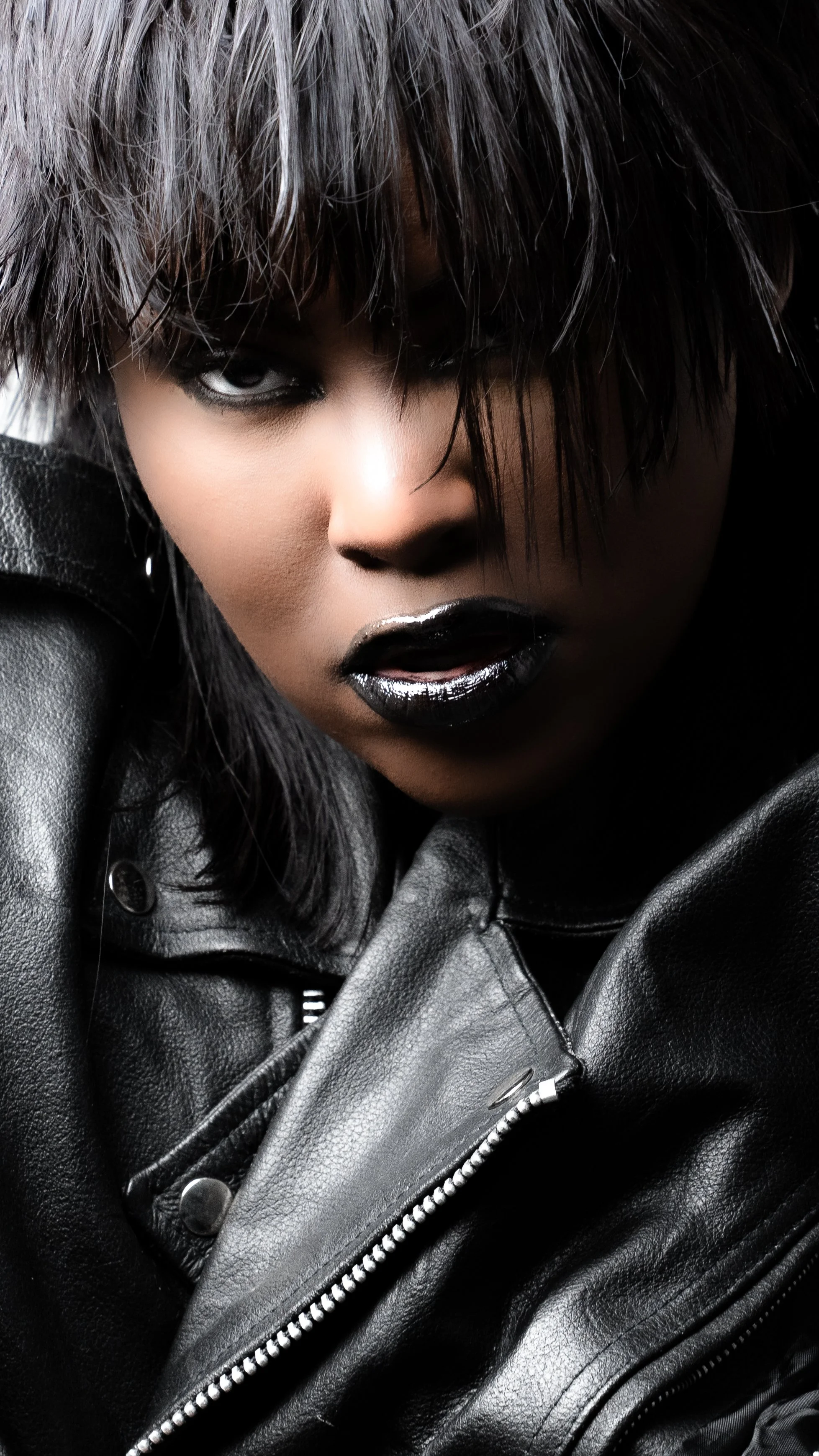 A black-and-white portrait of a woman with dark, tousled hair, looking down, her face partially obscured by strands of hair.