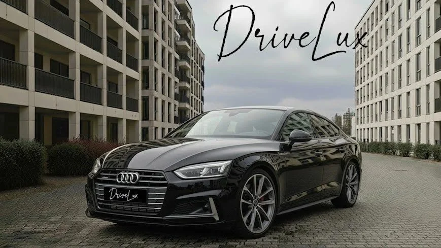 Voiture noire sport longue de marque Audi, stationnée entre deux immeubles résidentiels, avec le texte 'DriveLuxe' à l'avant et en haut à droite de l'image.