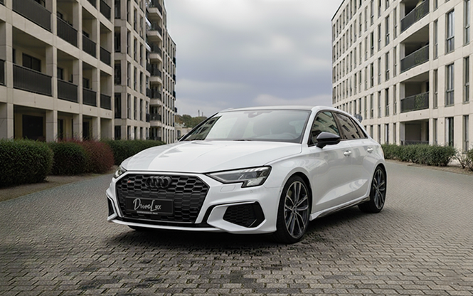 Voiture blanche Audi A3 garée dans une zone urbaine entre deux bâtiments modernes