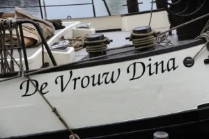 Close-up van een scheepsnaam "De Vrouw Dina" op de zijkant van een boot.